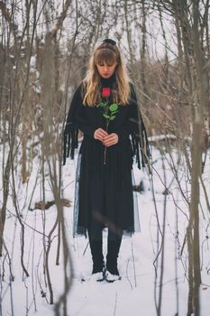 Lonely woman is standing in forest and holding red rose.