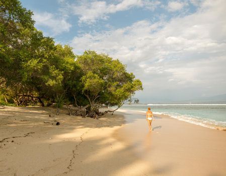 Young woman walking along tropical beach at Gili islands, Indonesia