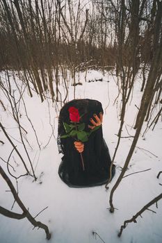 Lonely woman is kneeling in forest and holding red rose.