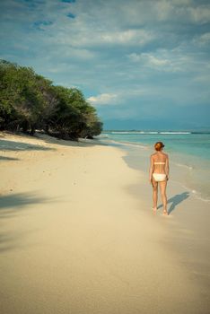 Young woman walking along tropical beach at Gili islands, Indonesia