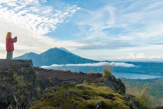 Young woman taking snapshot of lake Batur and mount Agung with her smartphone in Bali at sunrise