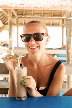 Young woman enjoying milkshake at tropical beach cafe