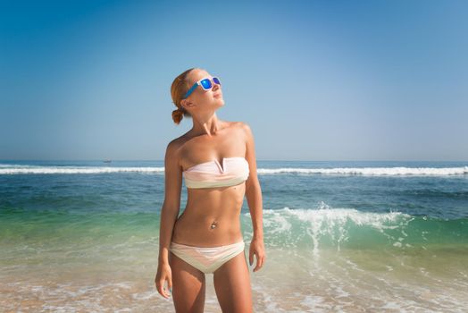 Young slim woman wearing bikini and sunglasses at the ocean beach