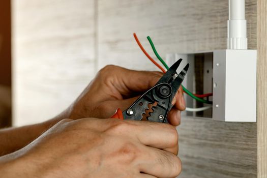 Electrician is stripping electrical wires in a plastic box on a wooden wall to install the electrical outlet.