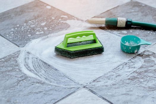 Close up the green plastic brush for scrubbing and cleaning the floor is placed on the wet tile floor and foamed with detergent.