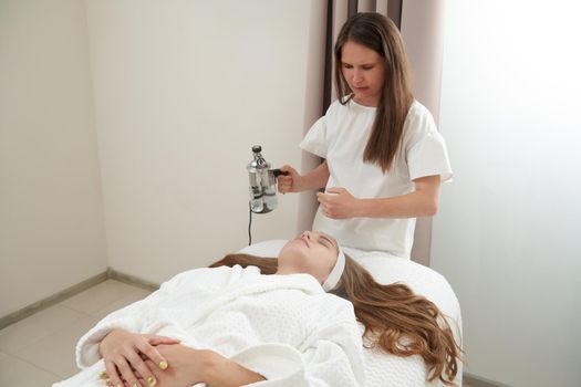 The procedure of steaming the skin of the face of a young woman before cleaning the skin in spa salon