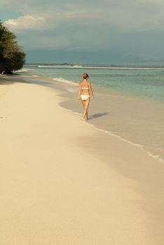 Young woman walking along tropical beach at Gili islands, Indonesia