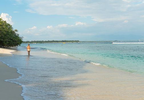 Young woman walking along tropical beach at Gili islands, Indonesia