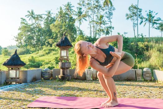 Young woman performing yoga asana at sunset with jungle background