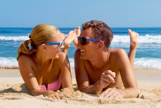 Happy couple having fun on the beach. Summer Vacation. Laughing Family enjoying Nature over Sea Background. Attractive Man and Woman at the Beach