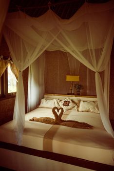 Bed with canopy and swans made of towels in bungalow