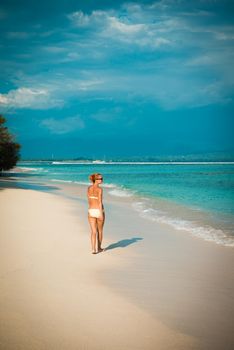 Young woman walking along tropical beach at Gili islands, Indonesia