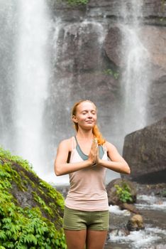 Young woman practicing yoga with waterfall in the background