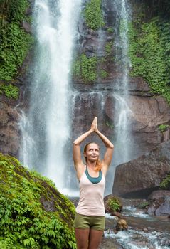 Young woman practicing yoga with waterfall in the background