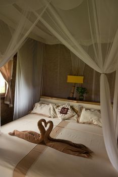 Bed with canopy and swans made of towels in bungalow