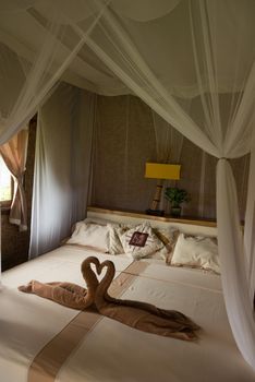Bed with canopy and swans made of towels in bungalow