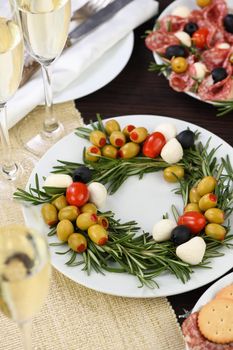 An appetizer of rosemary stuffed with olives with baby mozzarella and cherry tomatoes. Made in the form of a Christmas wreath.