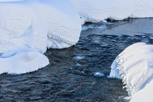 Stormy cold river passing through the snowdrifts under the ice. Mountain stream in winter