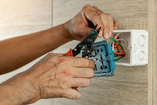 Electrician is stripping electrical wires in a plastic box on a wooden wall to install the electrical outlet.