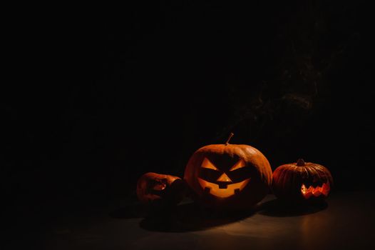 Pumpkins with carved grimaces and candles inside in the dark for halloween. Jack o latern in smoke