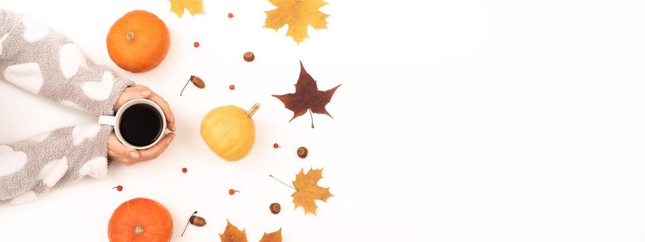 A woman holds a cup of black coffee near the yellow maple leaves of a pumpkin on a white background. Autumn flat lay