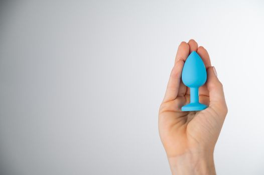 Woman holding a blue butt plug on a white background. Adult toy for alternative sex.