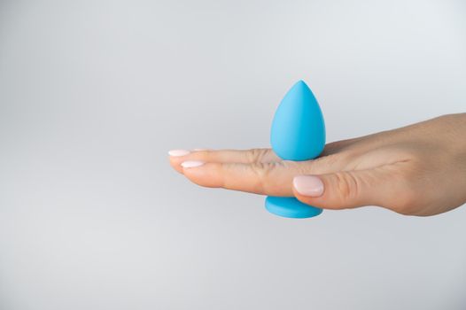 Woman holding a blue butt plug on a white background. Adult toy for alternative sex.