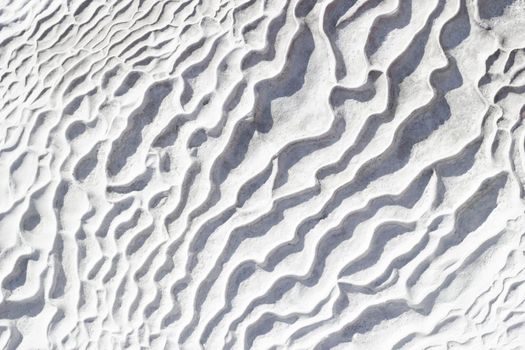 Gray-white texture background of Pamukkale calcium travertine in Turkey, pattern of diagonal waves, close-up.