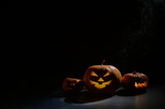 Pumpkins with carved grimaces and candles inside in the dark for halloween. Jack o latern in smoke