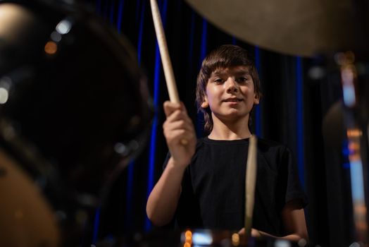 The boy learns to play the drums in the studio on a black background. Music school student.