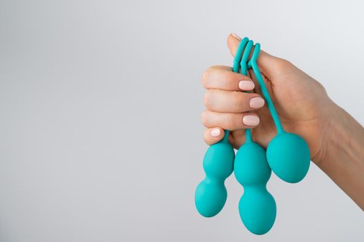 A faceless woman demonstrates a set of mint-colored vaginal balls. Girl holding a kegel trainer for training pelvic floor muscles on a white background