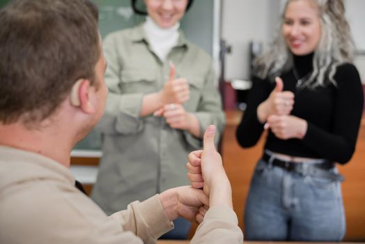 Two girls and a guy are talking in sign language. Three deaf students chatting in a university classroom