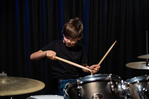 The boy learns to play the drums in the studio on a black background. Music school student.