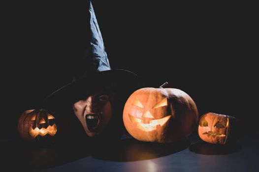 The head of an evil witch is on the table next to the glowing pumpkin jack-o-lantern.