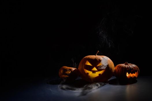 Pumpkins with carved grimaces and candles inside in the dark for halloween. Jack o latern in smoke