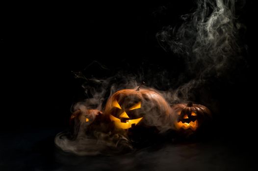 Pumpkins with carved grimaces and candles inside in the dark for halloween. Jack o latern in smoke