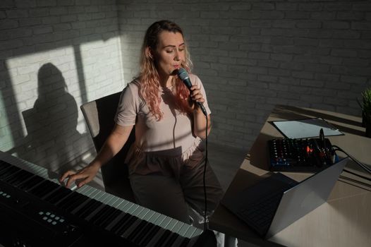A female blogger sings and plays the live electronic piano. Portrait of a girl recording a song on a web camera and composing on a synthesizer. Online music lessons. Distance learning in quarantine