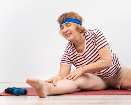 Elderly woman makes bends on a white background. Old lady doing health stretching exercises.