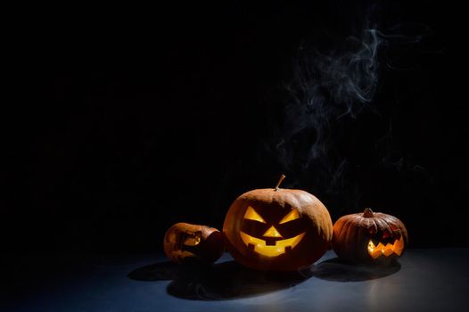 Pumpkins with carved grimaces and candles inside in the dark for halloween. Jack o latern in smoke