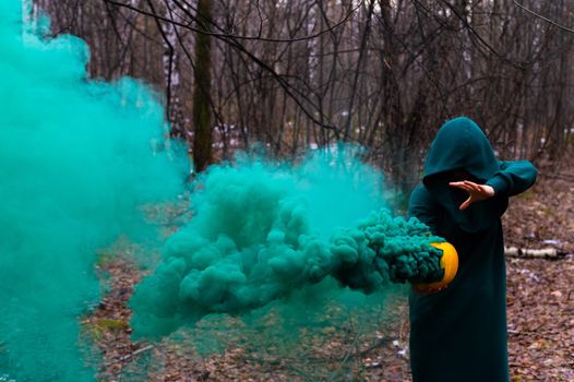 A creepy witch holds a steaming pumpkin in a deep forest. Jack o lantern with green smoke for halloween.