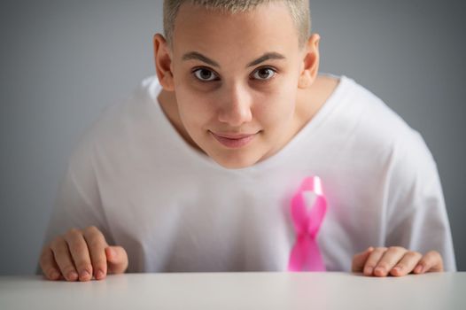 Woman with a short blonde haircut with a pink ribbon on a white t-shirt as a symbol of breast cancer on a white background