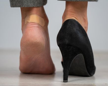 A woman in black shoes puts a plaster on a corn.