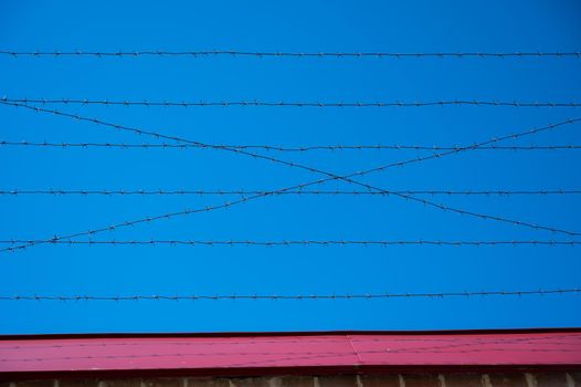 Barbed wire on the fence of the prison against the blue sky.