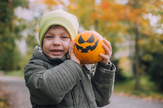 A boy with a Halloween pumpkin with eyes . The feast of fear. Halloween. An orange pumpkin with eyes. An article about Halloween.