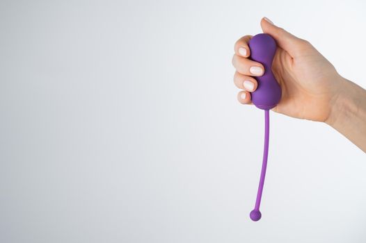 A faceless woman holding an electronic Kegel trainer for training pelvic floor muscles on a white background. Sex toy synchronized with a smartphone.