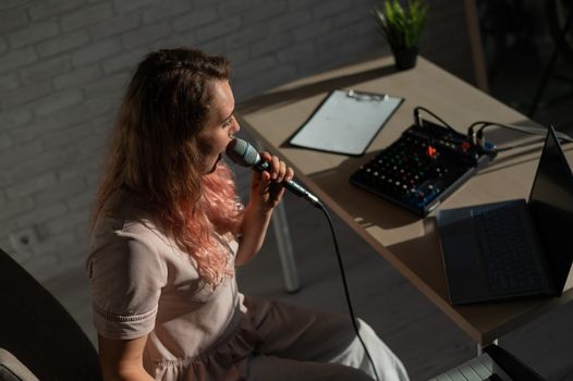 Expressive female singer has a video blog on a laptop. Portrait of a girl recording a song on a web camera and composing on a synthesizer. Online music lessons. Distance learning in quarantine