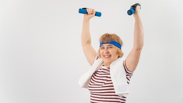 An elderly woman with a blue bandage on her head trains with dumbbells on a white background.