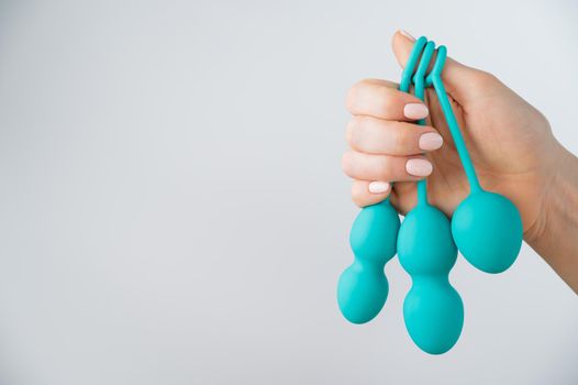 A faceless woman demonstrates a set of mint-colored vaginal balls. Girl holding a kegel trainer for training pelvic floor muscles on a white background