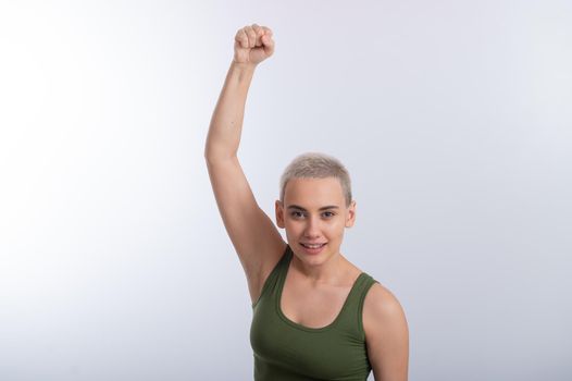 Young caucasian woman holding her fist up on a white background. A girl with short hair is fighting for rights.