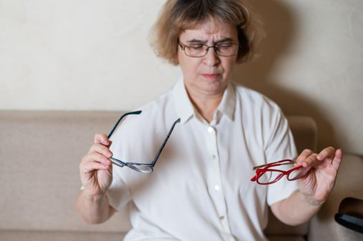 An elderly Caucasian woman chooses glasses from her home collection.